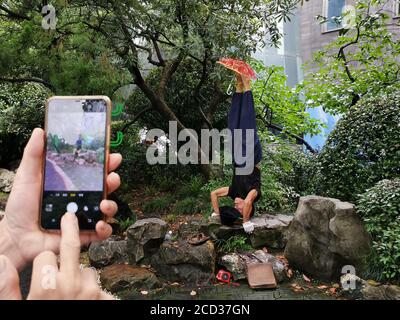 Herr Jiang, ein Mann in den Siebzigern, praktiziert Yoga auf besondere Weise, steht kopfüber mit dem Kopf und hält einen Schirm mit dem Fuß auf einem Ro Stockfoto