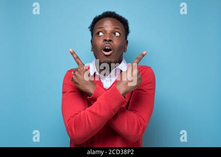 Der junge afrikaner zeigt seitwärts, versucht zwischen zwei Optionen zu wählen. Stockfoto