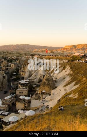 Goreme, Türkei, 3. September 2017: Abendansicht von oben auf eine kleine Stadt. Die Menschen versammelten sich auf dem Berg, um den Sonnenuntergang in der türkischen Kappadokien zu beobachten. Stockfoto