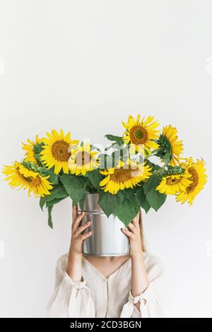 Schöne junge Frau in Leinenkleid hält Sonnenblumen Bouquet in einem Zinn Eimer auf weißem Hintergrund. Stockfoto