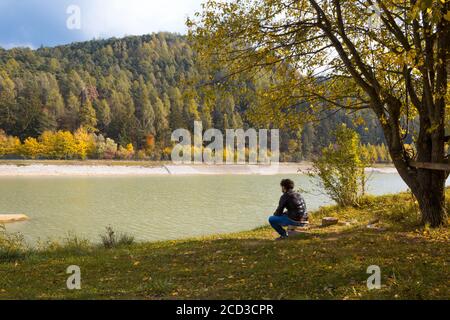 Landschaft mit jungen Mann sitzt allein unter einem Baum. Er blickt Berge und einen See in einem Herbsttag. Konzept der Entspannung und in der Natur zu verlieren. Stockfoto