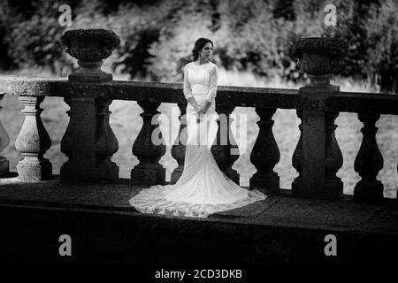 Eine schöne Braut in einem luxuriösen Kleid steht auf einem großen Balkon. Schwarzweiß-Foto Stockfoto