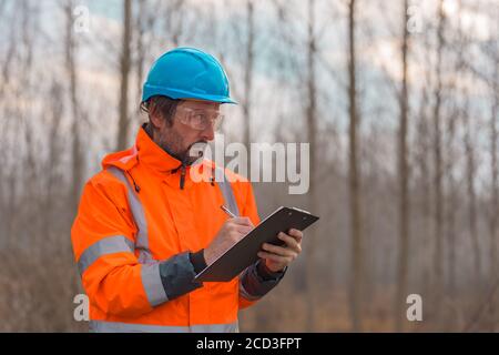 Forsttechniker sammelt Daten in Wald und schreibt Notizen auf Notizblock in der Zwischenablage Stockfoto