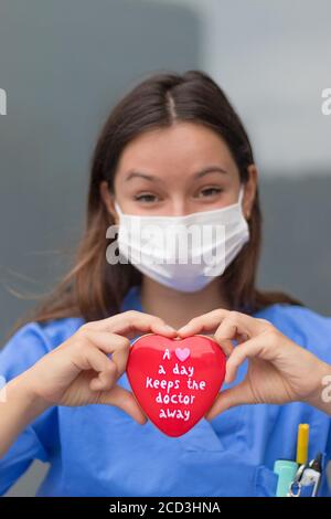 Eine Krankenschwester hält eine herzförmige Schachtel voller herzförmiger Süßigkeiten mit einem lustigen Spruch auf dem Deckel. Bilbao, Spanien Stockfoto