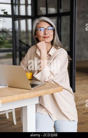 Foto von reifen träumen konzentrierte Geschäftsfrau drinnen zu Hause Mit Laptop-Computer Stockfoto
