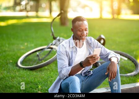 Funky afroamerikanischen Mann mit Fahrrad Surfen im Internet auf seine Smartphone im Stadtpark Stockfoto