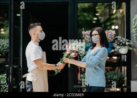 Kundenservice im Blumenladen. Mann in Schutzmaske gibt Blumenstrauß an Klient Stockfoto