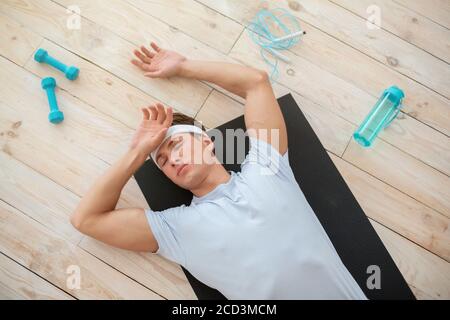 Heimtraining. Müder Mann, der mit Sportgeräten auf der Matte auf dem Boden liegt Stockfoto