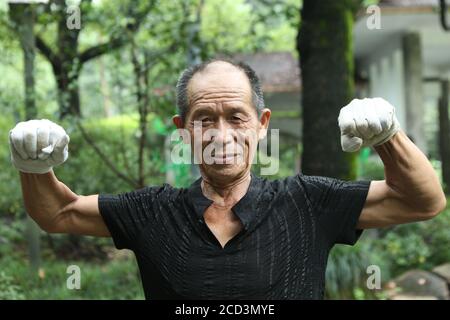 Herr Jiang, ein Mann in den Siebzigern, praktiziert Yoga auf besondere Weise, steht kopfüber mit dem Kopf und hält einen Schirm mit dem Fuß auf einem Ro Stockfoto