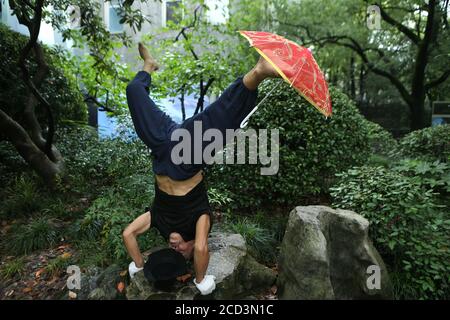 Herr Jiang, ein Mann in den Siebzigern, praktiziert Yoga auf besondere Weise, steht kopfüber mit dem Kopf und hält einen Schirm mit dem Fuß auf einem Ro Stockfoto