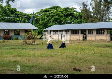 Pemba Island, Sansibar, Tansania - Januar 2020: Zwei Grundschüler halten ihr Buch auf dem Kopf und bewegen sich in Uniform durch den Schulhof Stockfoto