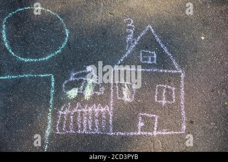 Kinder zeichnen mit Kreide auf dem Asphalt. Haus mit Rohr und Zaun und Auto im Hof. Glückliche Familie, Kindheit, süße Heimat. Handzeichnung mit Witz Stockfoto