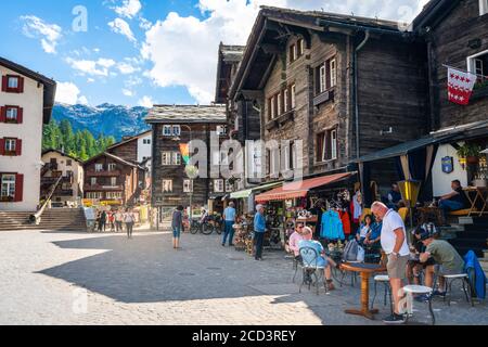 Zermatt Schweiz , 2. Juli 2020 : Café-Terrasse mit Touristen und alten Häusern im Sommer in Zermatt Schweiz Stockfoto