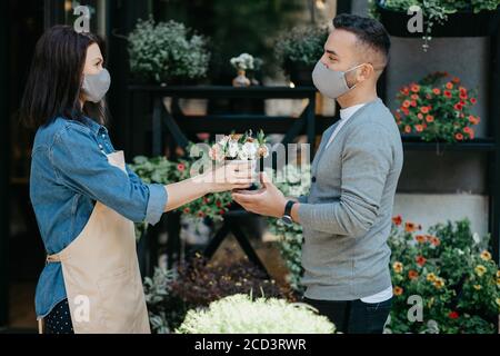 Verkauf von Pflanzen im Blumenladen. Frau in Schürze gibt wenig Blumenstrauß an Klient Stockfoto