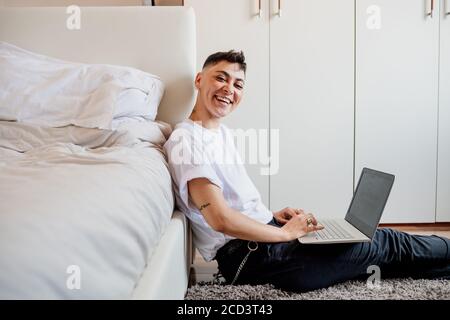 Junge Frau mit rasierten Kopf sitzt im Schlafzimmer, mit Laptop, lächelnd an der Kamera. Stockfoto