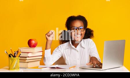 African American School Girl Bei Laptop Raising Hand, Gelber Hintergrund Stockfoto