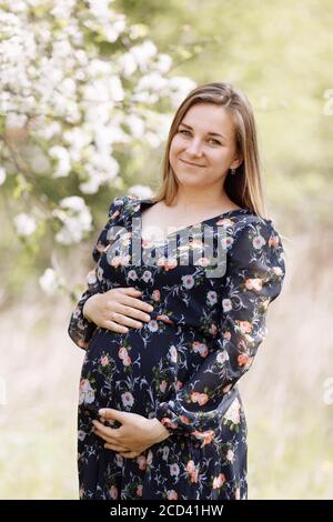 Eine schöne schwangere Frau im Frühling blühenden Park. Die werdende Mutter spaziert im Frühlingsgarten. Warten auf ein Wunder. Stockfoto