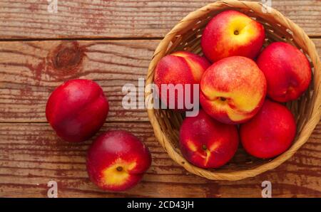 Nektarine. Reife saftige Bio-Nektarinen (Pfirsiche) in einem Weidenkorb. Ganze Früchte auf einem Holztisch. Selektiver Fokus, Draufsicht, Kopierbereich Stockfoto