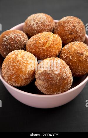 Hausgemachte gebratene Donut Löcher in einer rosa Schale auf schwarzem Hintergrund, niedrige Winkel Ansicht. Nahaufnahme. Stockfoto