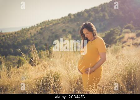 Schwangere glückliche Frau berührt ihren Bauch. In voller Länge schwangere Schönheit junge Mutter im Freien Porträt, streicheln ihren Bauch und lächeln. Gesunde Schwangerschaft Stockfoto