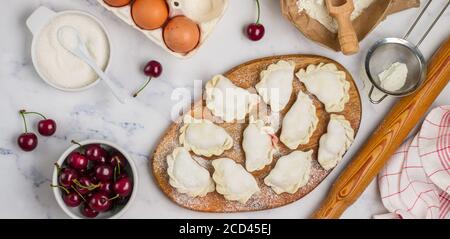 Bereiten Sie köstliche süße Knödel mit Kirschen. Traditionelles russisches und ukrainisches Dessert. Vareniki und Zutaten auf dem Marmorboden -Mehl, Stockfoto