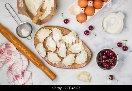 Bereiten Sie köstliche süße Knödel mit Kirschen. Traditionelles russisches und ukrainisches Dessert. Vareniki und Zutaten auf dem Marmorboden -Mehl, Stockfoto