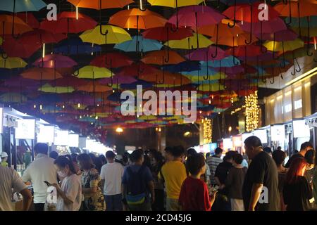 Die Menschen gehen unter einem Korridor, der mit bunten Regenschirmen geschmückt ist und den Nachtmarkt in Shenyang, im nordöstlichen Teil von Liao, ankurbeln soll Stockfoto