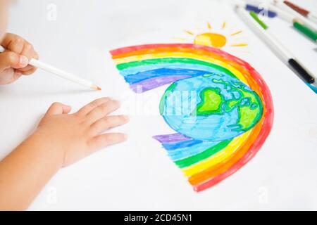 Das Kind zeichnet einen Planeten der Welt mit Regenbogen und Sonne auf das weiße Papier. Kinderzeichnungen, Gemälde und Konzepte. Bildung und Kunst Stockfoto