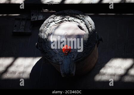 Flüssiges rotes heißes Metall in Metallurgieeimer. Metallurgische Werkshalle. Graue Schlacke auf dem Eimer. Nahaufnahme Stockfoto