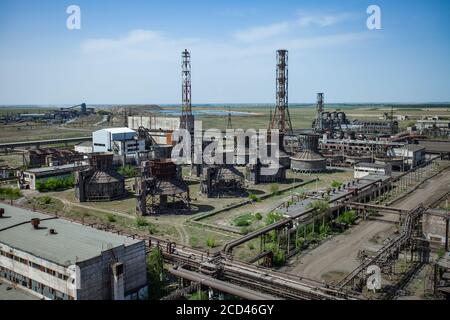 Veraltete sowjetische Metallurgie Fabrikgebäude und verrostete Rohrleitungen und Kamine und Kühltürme in Steppe auf blauem Himmel Hintergrund. Taraz Stadt. Stockfoto