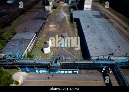 Alte kaputte sowjetische Metallurgie Fabrikgebäude mit Pipelines, weißen Tanks und kleinen blauen Gebäuden. Vogelperspektive und Tilt-Shift. Taraz Stadt. Stockfoto