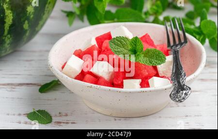Köstlicher Salat aus Wassermelone, Feta-Käse und Minze. Ein erfrischender Sommer-Gourmet-Snack auf einem weißen Teller auf einem Holztisch. Selektiver Fokus Stockfoto
