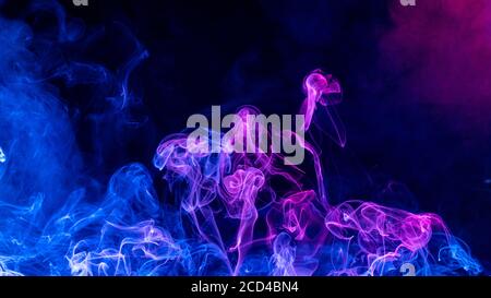 Konzeptuelles Bild von mehrfarbigem Rauch isoliert auf dunkelschwarzem Hintergrund, Halloween Design-Element. Stockfoto