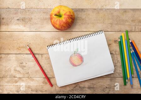 Kinderzeichnung, Apfel und Buntstifte. Holztisch. Draufsicht Stockfoto
