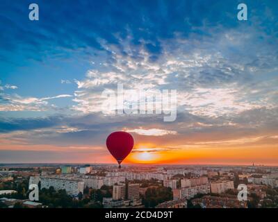 Roter Heißluftballon fliegt über kleine europäische Stadt bei Sommersonnenaufgang, Kiev Region, Ukraine Stockfoto