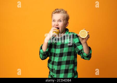 Saures Gesicht, fröhlicher Gesichtsausdruck. Der Junge beißt eine Zitrone. Glückliches Kind, Mimik, Energie und Spaß. Ausdruck und Freude des Kindes. Die bo Stockfoto