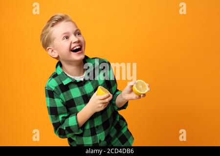 Saures Gesicht, fröhlicher Gesichtsausdruck. Der Junge beißt eine Zitrone. Glückliches Kind, Mimik, Energie und Spaß. Ausdruck und Freude des Kindes. Die bo Stockfoto