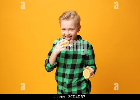 Saures Gesicht, fröhlicher Gesichtsausdruck. Der Junge beißt eine Zitrone. Glückliches Kind, Mimik, Energie und Spaß. Ausdruck und Freude des Kindes. Die bo Stockfoto