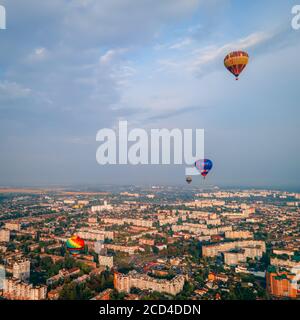 Bunte Heißluftballons fliegen über kleine europäische Stadt bei Sommeruntergang, Kiew Region, Ukraine Stockfoto
