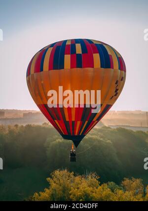 Bunte Heißluftballon hebt ab von grünen Park in kleinen europäischen Stadt bei Sommersonnenaufgang, Kiew Region, Ukraine Stockfoto