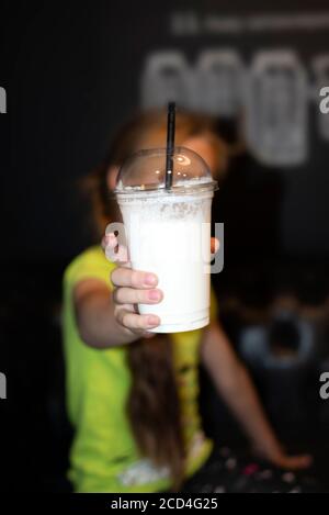 Kleines Mädchen in einem Café hält einen Milchshake direkt an die Kamera. Teenager-Mädchen trinken Milch Cocktail Stockfoto