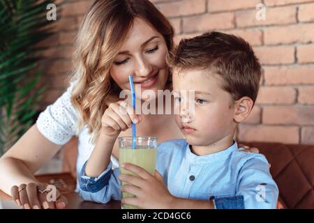 Mama wacht über ihren Sohn im Café. Sohn trinkt alkoholfreies Getränk Stockfoto