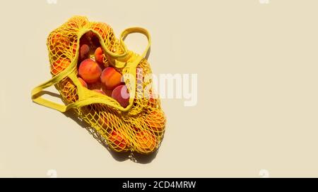 Reife Pfirsiche in einem Netzbeutel oder Saitenbeutel auf hellgelbem Hintergrund. Flach liegend. Keine Verschwendung. Stockfoto