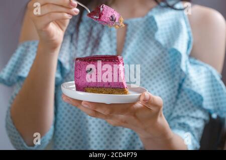 Ein Stück Blaubeergeschmack Käsekuchen mit Heidelbeersauce auf einem Kekscrumb, Bäckerei. Köstliche Scheibe Blaubeeren Käsekuchen in Frau Hand Stockfoto