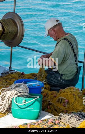 Ein alter griechischer Fischer, der Netze auf einem Boot ausbessert, das im Hafen bei Zante zakynthos Stadt in griechenland festgemacht ist. Stockfoto