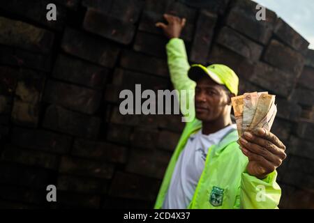 Ein kolumbianischer Holzhändler hält Banknoten, während er im Hafen von Turbo, Kolumbien, rohes Schnittholz verkauft, das aus dem pazifischen Regenwald gewonnen wird. Stockfoto