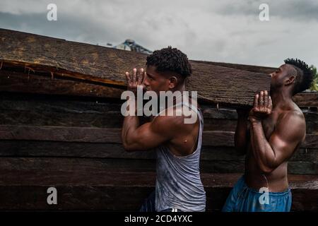 Afro-kolumbianische Träger heben ein grobes Schnittholz, das aus dem pazifischen Regenwald gewonnen wird, während des Holztransports im Hafen von Turbo, Kolumbien. Stockfoto