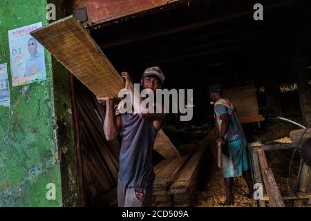 Ein kolumbianischer Arbeiter trägt bei der Holzbearbeitung in einem Sägewerk in Quibdó, Kolumbien, ein grobes Schnittbrett, das aus dem pazifischen Regenwald gewonnen wird. Stockfoto