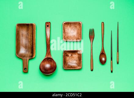 Oben mit hölzernen Küchengeräten isoliert auf einem grünen Hintergrund. Holzteller, Löffel, Gabeln und Essstäbchen, flach liegend. Stockfoto