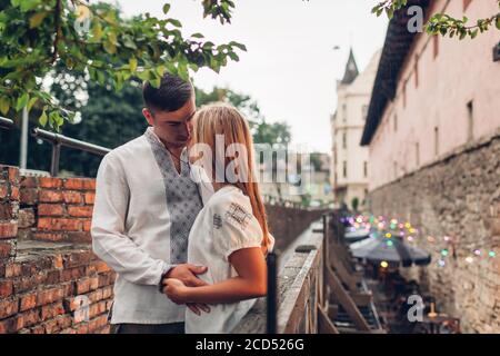 Liebevolles Paar, das in der Altstadt von Lviv in traditionellen ukrainischen Hemden herumläuft. Die Menschen umarmen sich entspannt durch Arsenal unter Regen Stockfoto